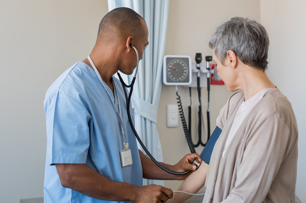 Male nurse checking blood pressure of a senior woman in medical office. African doctor taking the blood pressure of his patient at hospital. Young doctor measuring the blood pressure of mature woman.