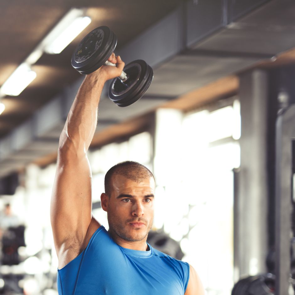 Young muscular man lifting up dumbbells at the gym.