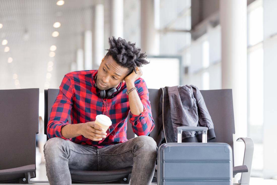 Man in airport going without sleep holding takeaway coffee looking tired
