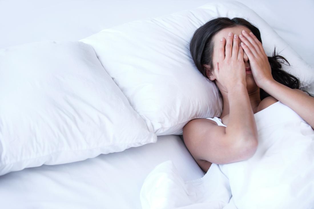 Woman in bed going without sleep suffering from insomnia covering eyes with hands